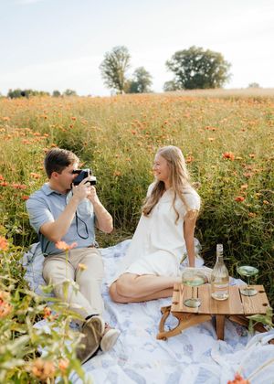 Romantic picnic setup with camera and drinks in flowering meadow.