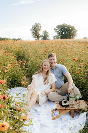 Couple shares laughs during picnic in wildflower field with vintage camera.