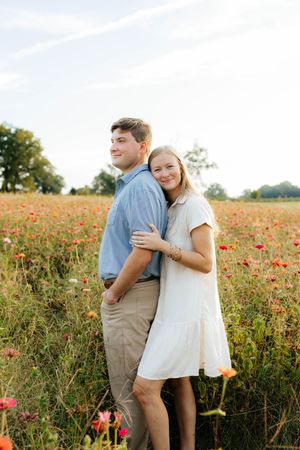 A couple embraces in a field of red poppies during golden hour with trees in the background.