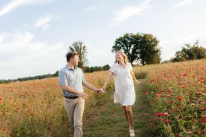 Couple dancing and laughing together in a field of red poppies during sunset.