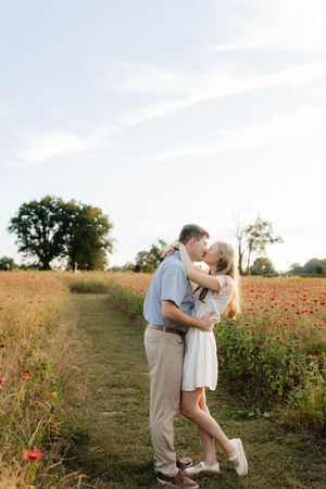 Couple sharing intimate moment on path through wildflower field at sunset.