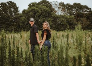 A couple poses playfully in a tall green field during a summer photoshoot.