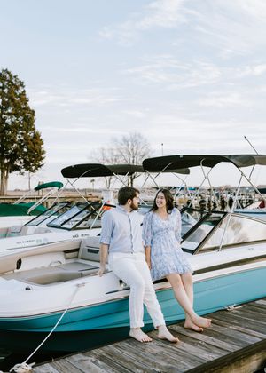 A couple in coordinated blue and white outfits stands on a dock surrounded by boats on a sunny day.