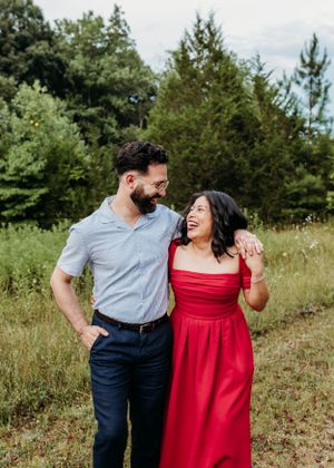 A couple laughs together in a field wearing red dress and blue casual attire.