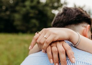 Close-up of hands with engagement rings resting on blue striped fabric.