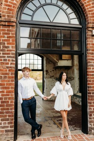 A couple playfully walks through brick archways in contrasting white and navy outfits.