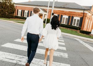 A couple walks across a crosswalk holding hands in coordinated outfits.