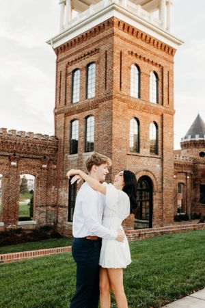 A couple shares romantic moments outside a historic brick tower building.