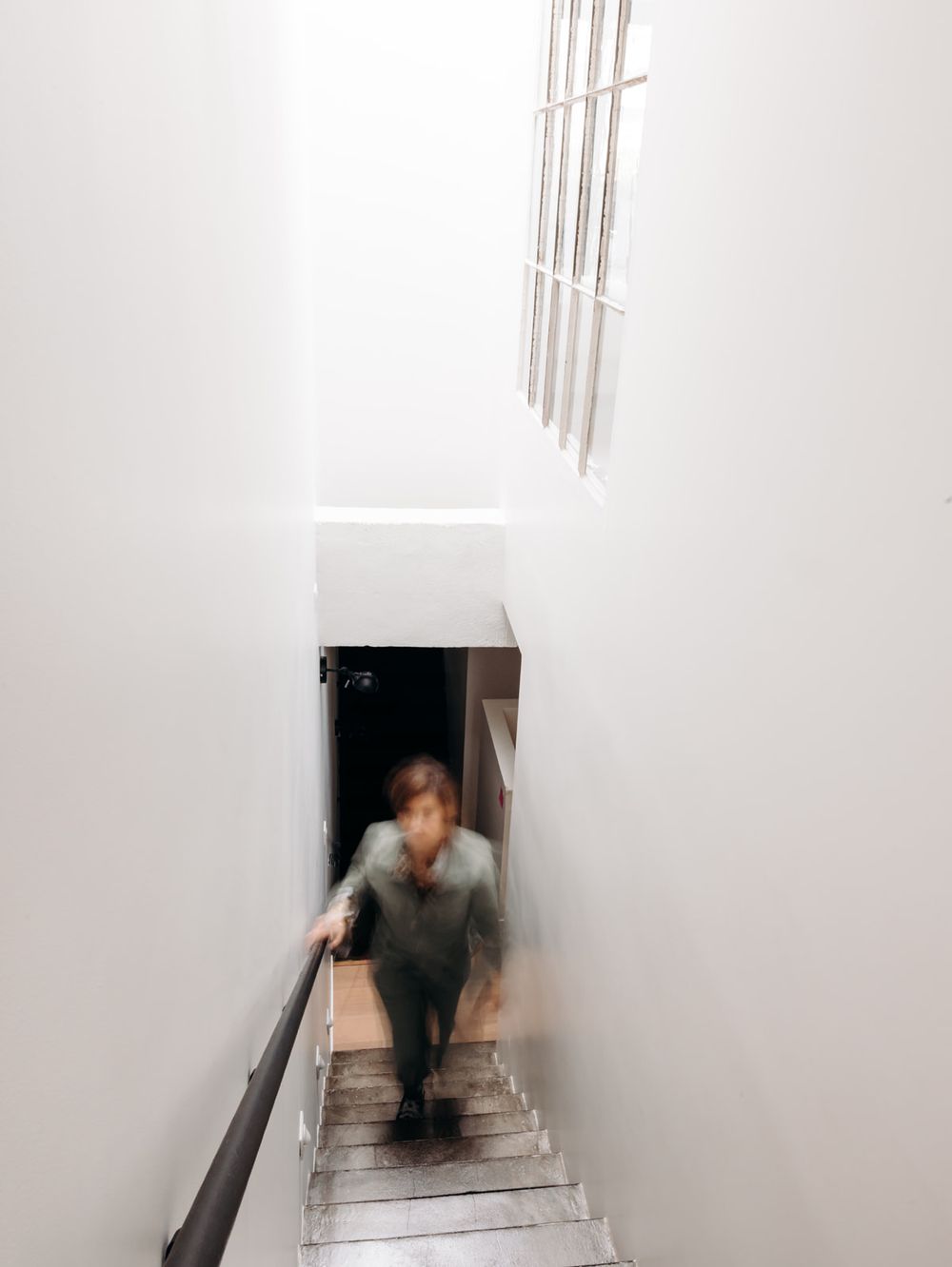 Blurred motion shot of a person ascending white minimalist staircase with natural light from above window.
