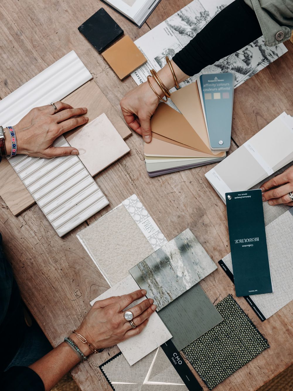 Interior designers reviewing material samples, color swatches, and fabric tiles on a wooden table during a design consultation.