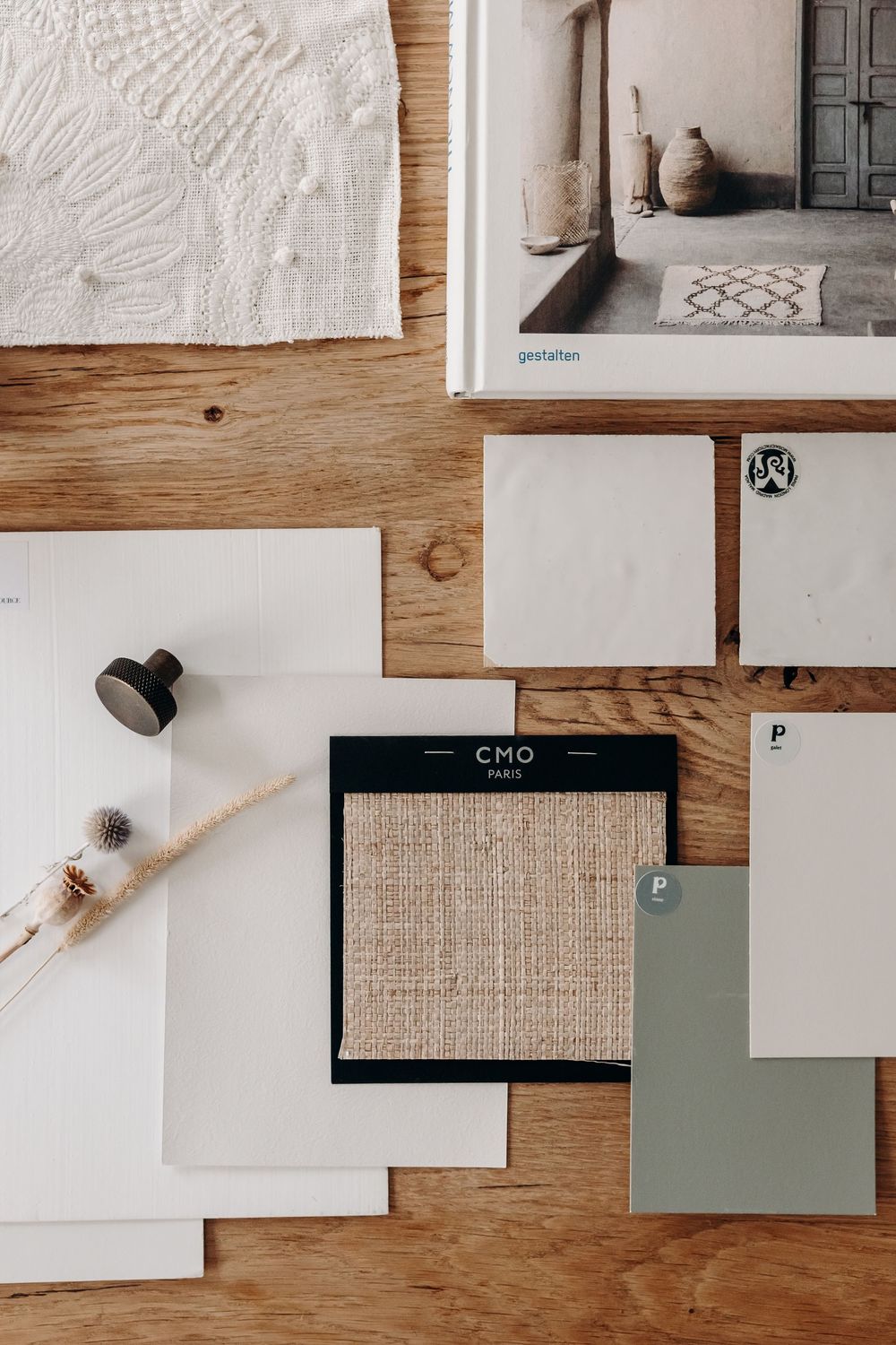 Flat lay mood board on wood with fabric swatches, paint samples, texture cards, and a design book for interior styling.