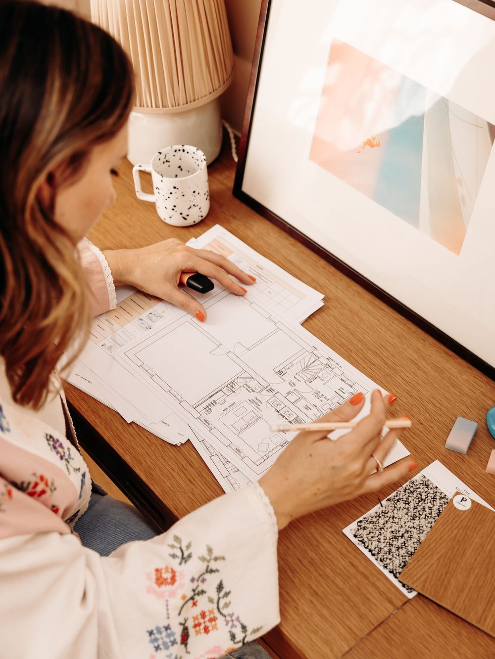 Woman reviewing architectural floor plans at a wooden desk with a speckled mug nearby.
