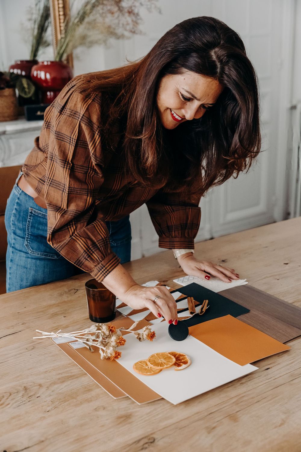Woman in plaid shirt arranging dried oranges and color swatches on a wooden table for a creative flat lay project.