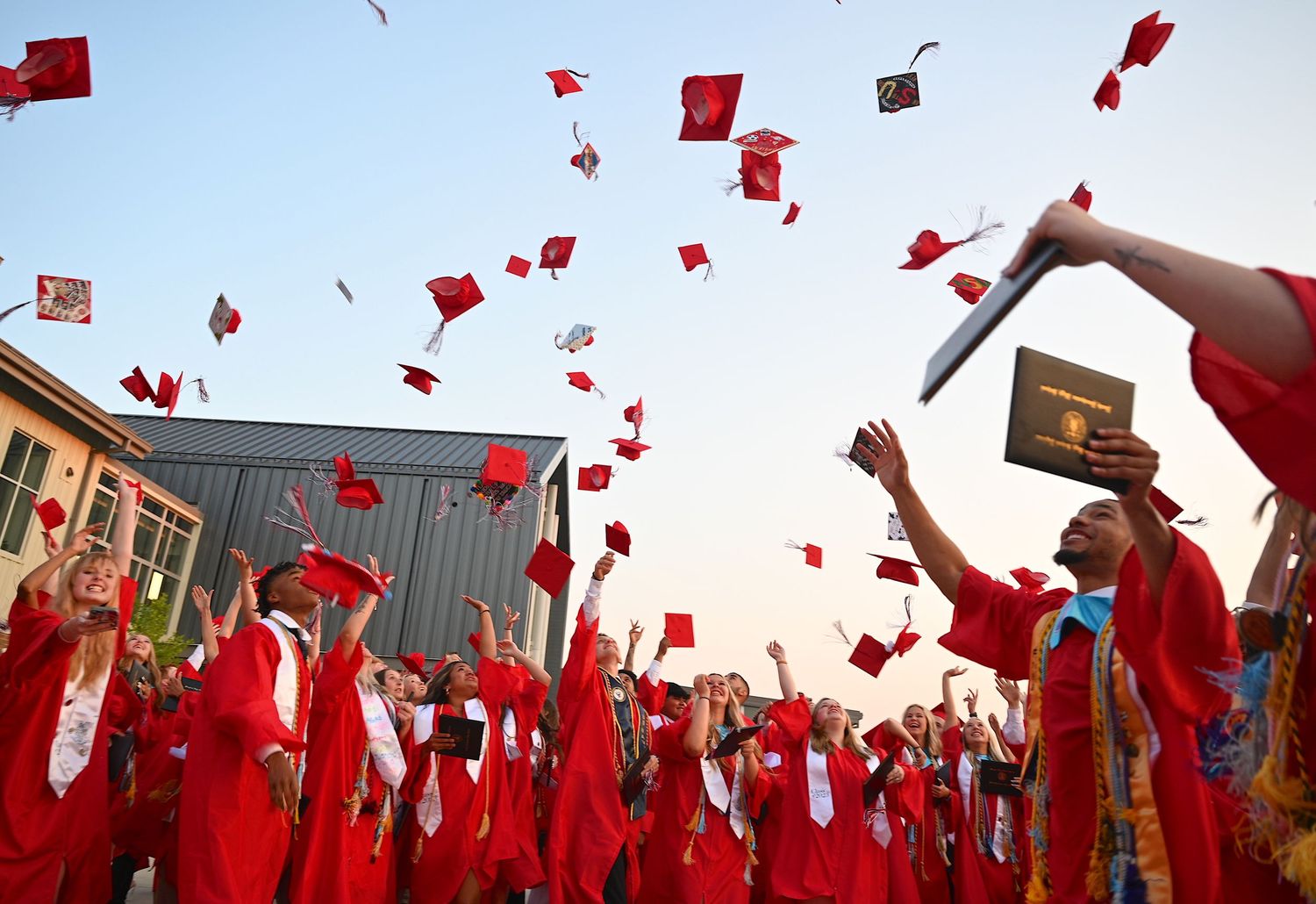 Graduates in bright red caps and gowns toss their mortarboards into the air during an outdoor graduation ceremony.