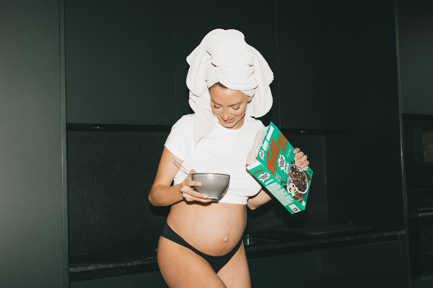 Gravid kvinna häller upp cornflakes och skrattar i sitt kök