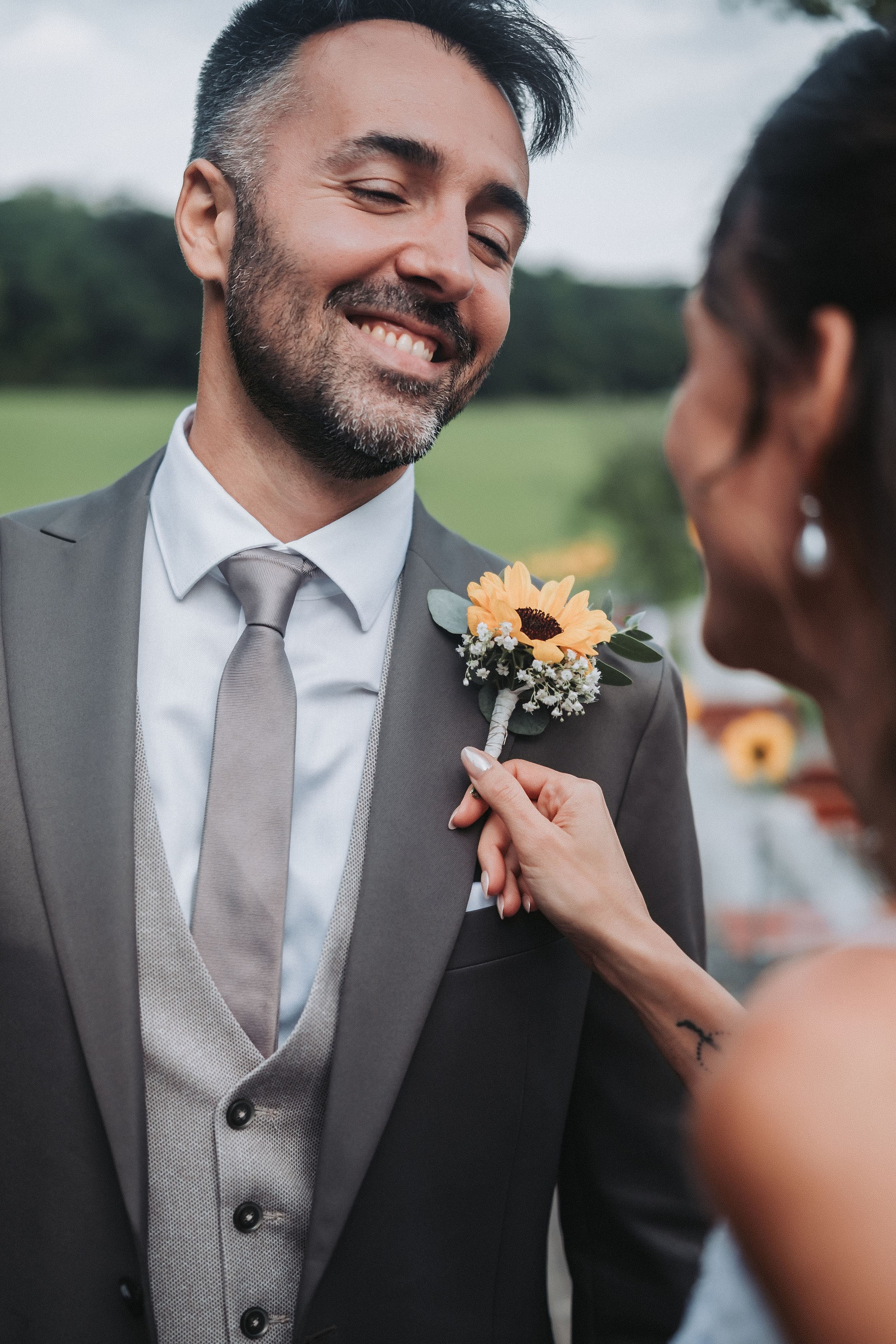 A sequence of wedding moments showing a groom getting his boutonniere pinned on his grey suit jacket.