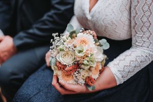 Delicate wedding bouquet with blush roses, baby's breath and greenery rests in hands wearing lace sleeves.