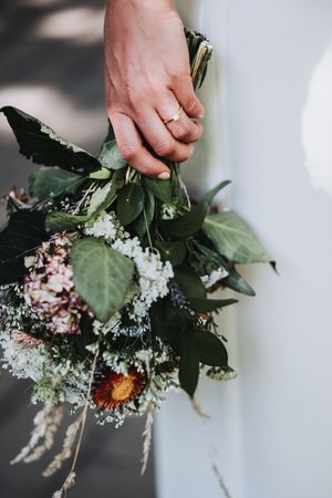 Hands arranging a delicate bouquet of white flowers and greenery against a soft, blurred background.
