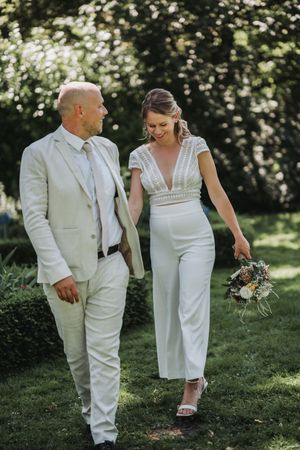 Couple in matching white outfits walking together on lush green grass during an outdoor summer celebration.