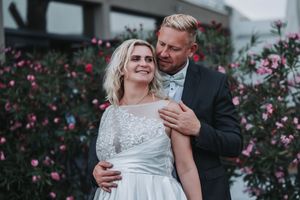 A romantic couple shares an intimate moment in front of pink flowering bushes during their wedding photoshoot.