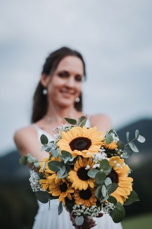 A wedding bouquet featuring bright yellow sunflowers with eucalyptus leaves against a cloudy sky background.