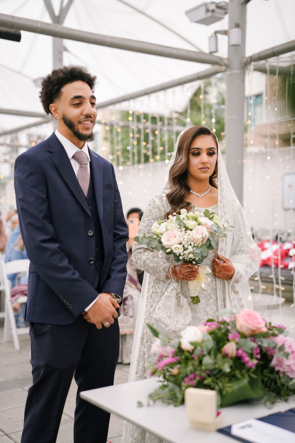 Newlywed couple shares joyful moments during their wedding ceremony under a white tent with floral decorations.