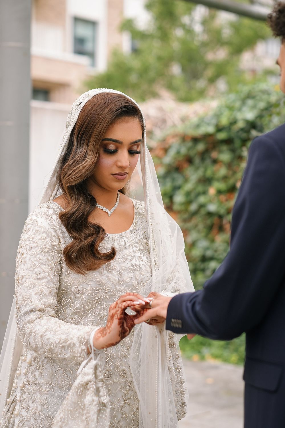 A couple exchanges rings during a wedding ceremony against a backdrop of green foliage.