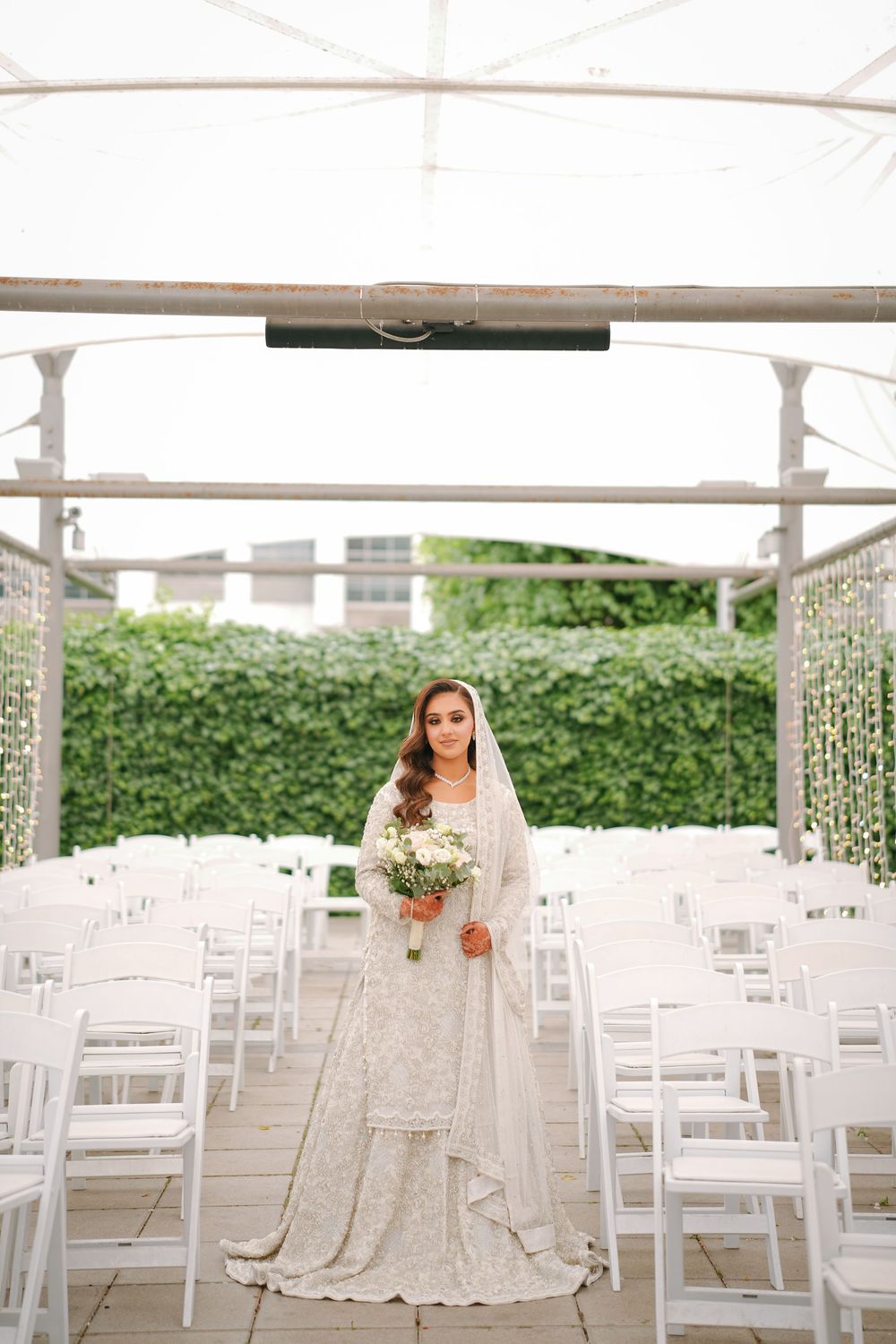 An outdoor wedding ceremony setup with white folding chairs arranged in rows under an elegant covered pavilion.