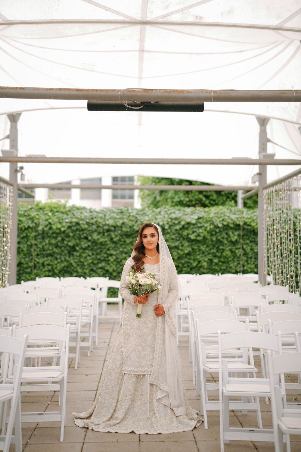 Elegant white chairs and tables arranged under a tent canopy for an outdoor wedding reception with floral decor.