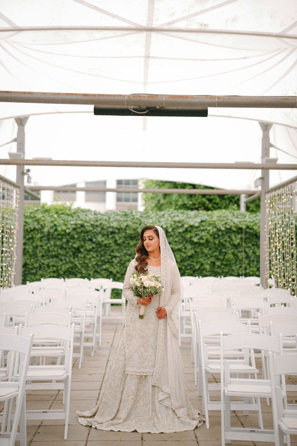 A modern outdoor wedding ceremony setup with white folding chairs and draped fabric under an elegant tent canopy.