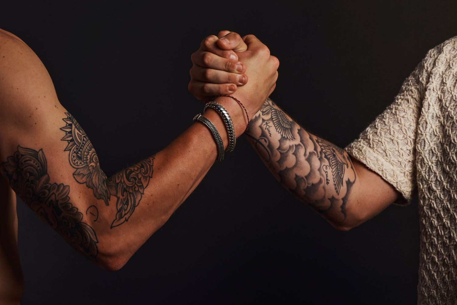 Close-up van twee getatoeëerde armen met een sterke handdruk.