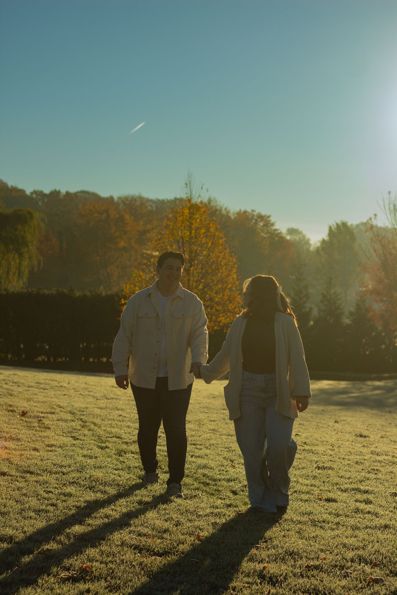 Two silhouettes walk together across a sunlit autumn field casting long shadows in the golden evening light.