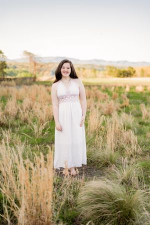 A person in a flowy white dress poses gracefully in a golden grass field during sunset.