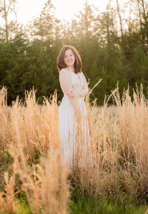 Someone in a white dress poses gracefully in a golden field of tall grass during sunset.