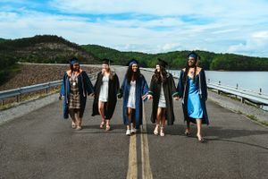 Group of high school seniors walk together on road with mountain lake and blue sky in background.