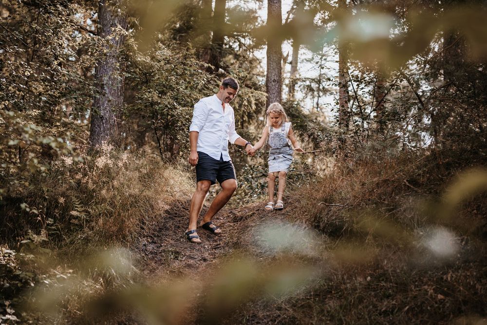 A family enjoys a playful moment together in a sunlit wooded area.