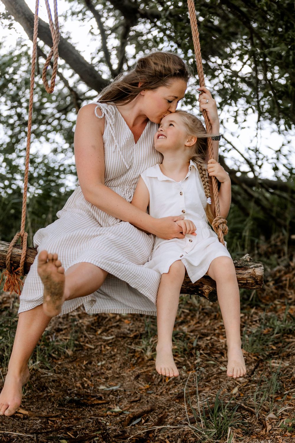 Two people share a tender moment while sitting on a wooden swing in a forest setting.