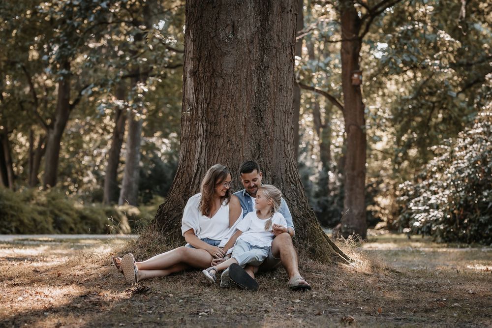 Family sitting together at base of large tree in wooded setting.