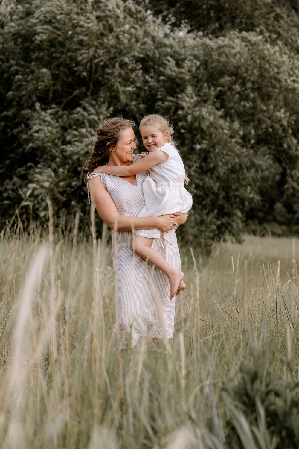 A sweet embrace captured in a field of tall grass during golden hour.