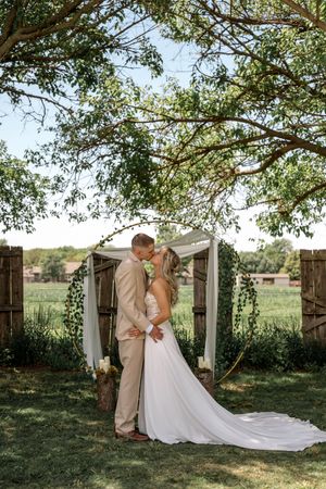 Romantic wedding scene under a white archway decorated with greenery in an outdoor garden setting during golden hour.