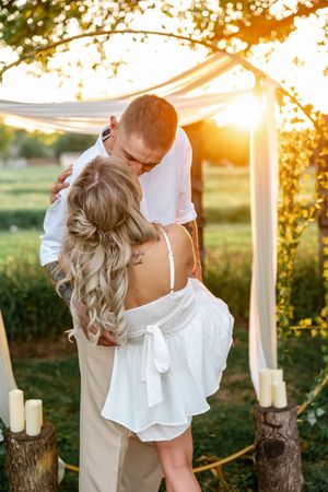 A romantic outdoor wedding ceremony at sunset with white draped fabric and rustic candle decor.