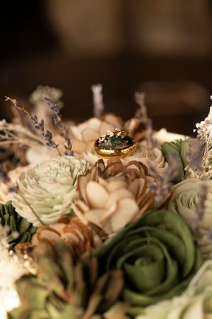 Wedding rings nestled among soft beige and sage green roses in an elegant floral arrangement.