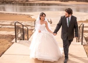 A couple walks down concrete steps near a waterfront on their wedding day.