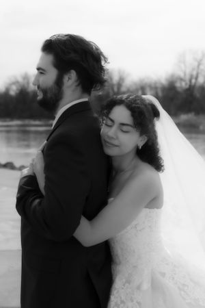 A black and white portrait of a couple embracing during their wedding celebration by a lake.