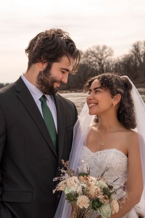 A joyful couple shares an intimate moment on their wedding day with winter trees in the background.