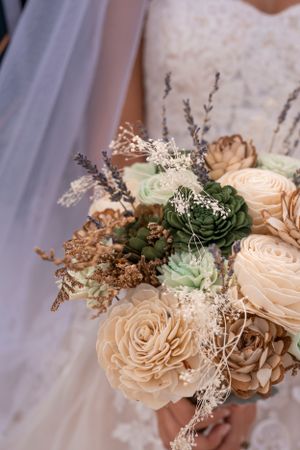 A romantic wedding bouquet with peach roses, green succulents, and delicate baby's breath against a light background.