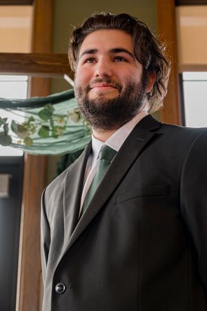 A groom in a black suit with a sage green tie smiles warmly at the camera.