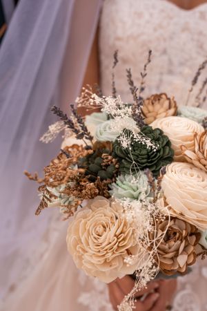 A delicate wedding bouquet with peach roses, green succulents, dried flowers and baby's breath against white fabric.