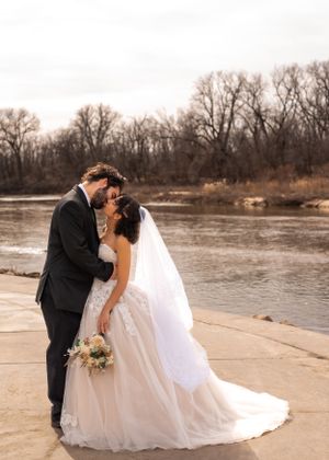 Elegant wedding photo at the riverside showing a couple sharing an intimate moment against bare winter trees.