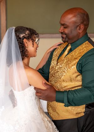 A couple shares an intimate moment during a wedding, with the groom wearing a gold vest and green shirt.
